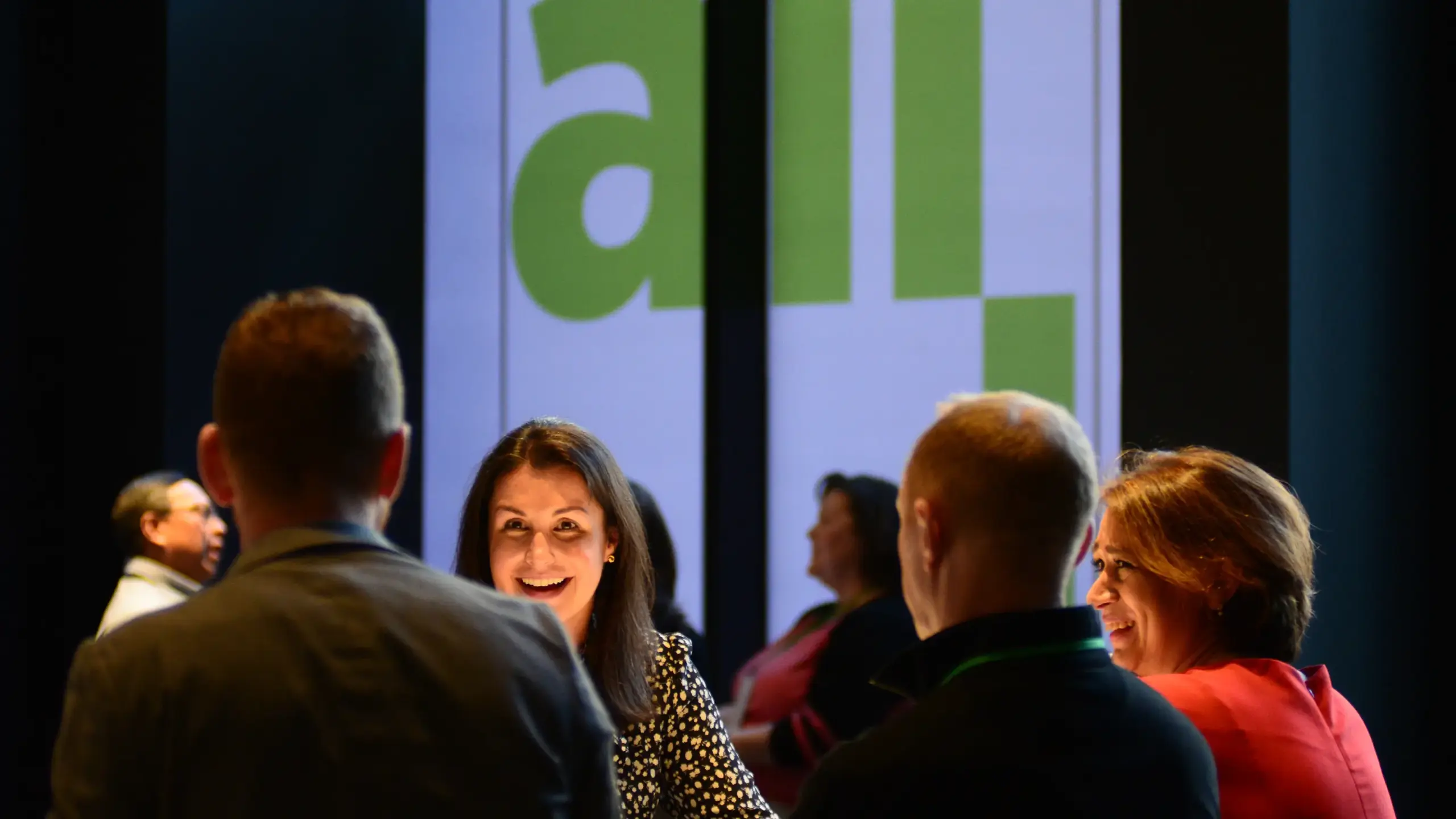 Woman with collegues in the lobby with All In logo signage behind her