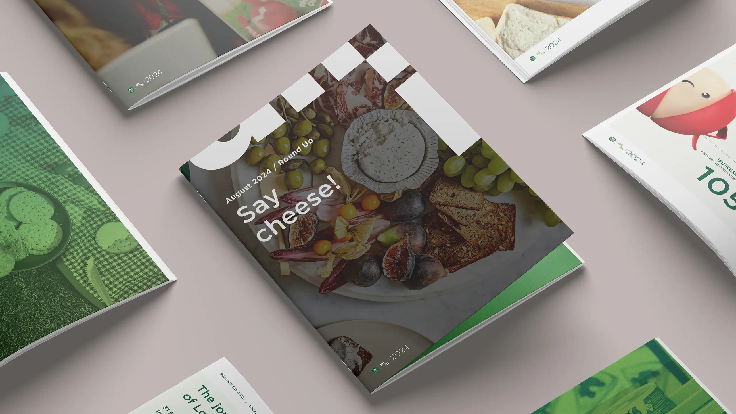 Angled mockups of Bel Brands’ ‘Say Cheese!’ August 2024 Round Up brochure featuring a cheese board with grapes, figs, and crackers