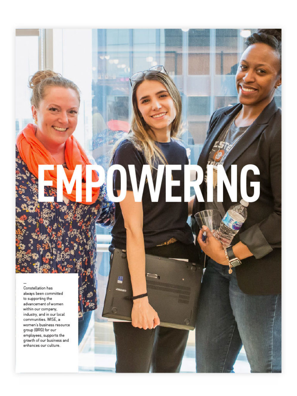 Three women smiling together indoors, one holding a laptop, against a backdrop of a bright window with the word "Empowering" prominently displayed.