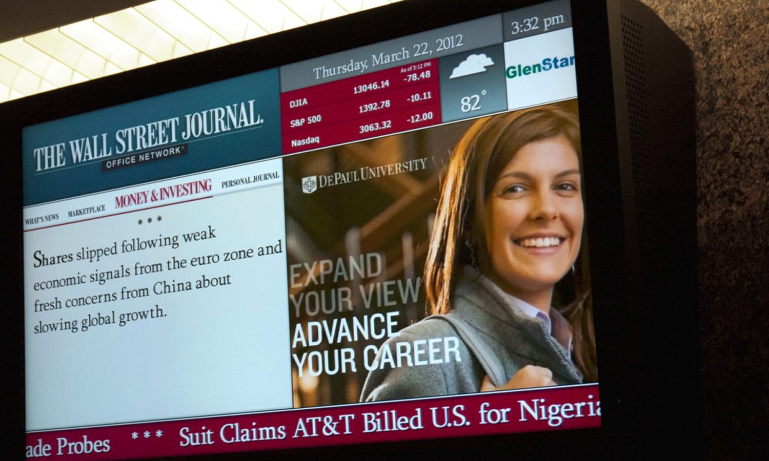 An electronic display shows The Wall Street Journal with a headline about economic concerns. Next to it, a DePaul University ad features a smiling woman with bold text saying, "Expand your view, advance your career."